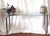 Tubular chrome console table or sofa with a uniquely styled hairpin or paper clip turn base. Has a glass top that is...