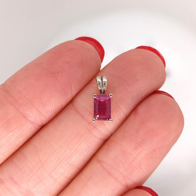 A ruby glows with red brilliance at the heart of this emerald cut pendant. Hand-set in solid 14K white gold, it balances...