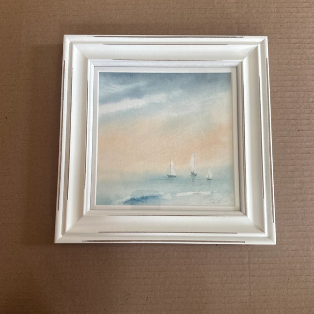 A soft, peaceful seascape watercolor capturing three sailboats gliding quietly across tranquil waters under a misty,...
