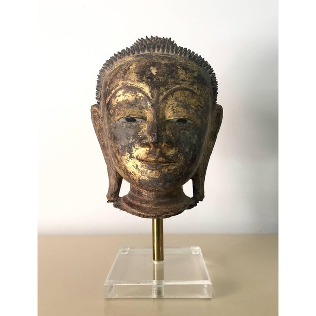 An gilt and lacquered wood Buddha head with displayed on a metal and Lucite stand. stunning presence with its refined...
