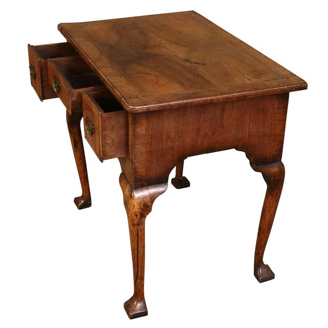This early 18th-century walnut lowboy features cabriole legs, pad feet, and feather-banded drawers with an elegant arched...