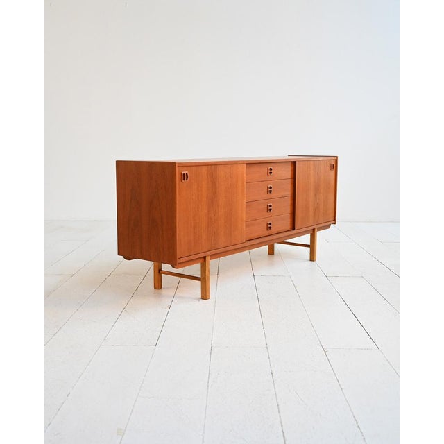 Scandinavian teak sideboard with sliding doors, four central drawers, and carved wooden handles. Swedish production from...