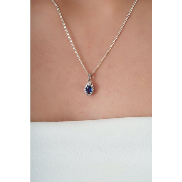 This halo pendant features a 0.55 carat oval-cut blue sapphire set in 14K white gold. The sapphire masuring 4.2 x 6 mm in...