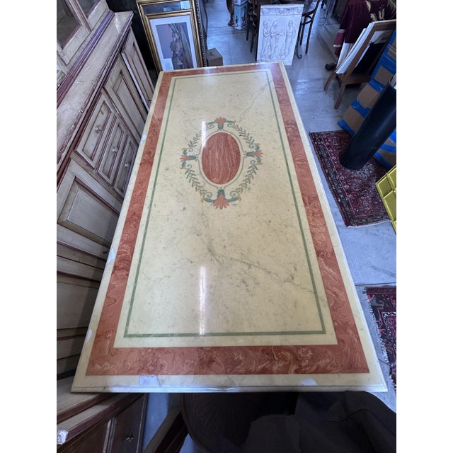 Inlaid dining table with crown decorations and marble pedestal bases. The rectangular top features a central inlay and...