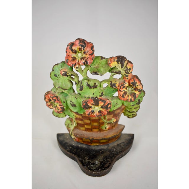 A vintage Hubley cast iron doorstop showing a geranium plant set inside a woven checkered flower pot on an iron plinth....