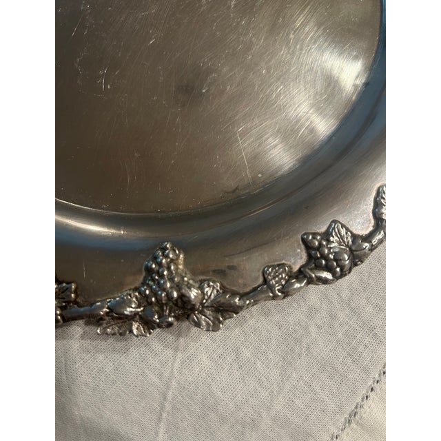 Vintage silver-tone serving platter featuring a richly detailed grapevine border with sculpted clusters of grapes and vine...