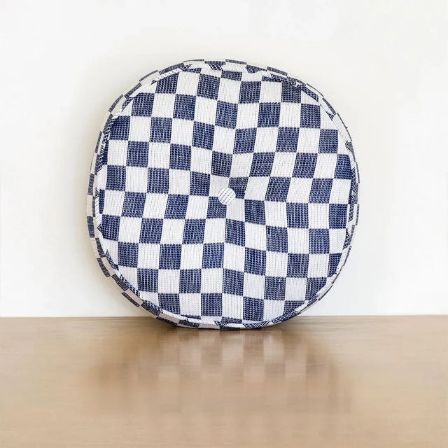 Circular pillow made from vintage blue and white checkered cotton fabric with edge piping and center button detailing.