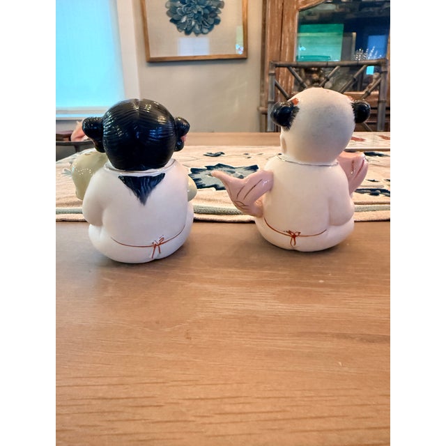 Two adorable figurines in the shape of a boy and girl. The boy is holding a pink koi fish and the girl is holding a yellow...