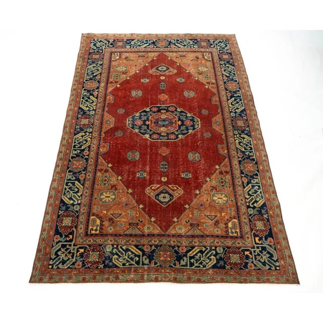 A striking antique Persian Serapi Heriz-style rug with a beautifully aged rust-red field, bold central medallion, warm...