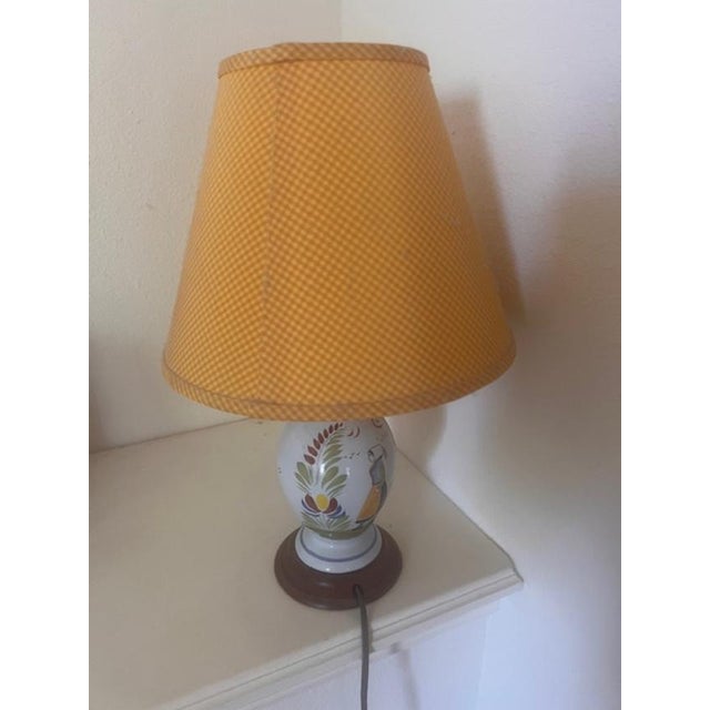 This vintage table lamp features a rounded ceramic base with hand-painted folk-style floral motifs. It is topped with a...