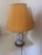 This vintage table lamp features a rounded ceramic base with hand-painted folk-style floral motifs. It is topped with a...