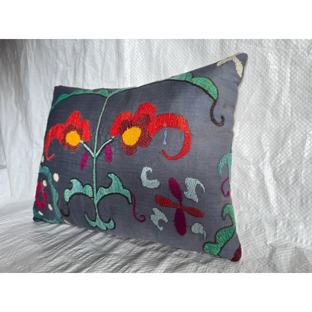 A striking vintage Suzani pillow showcasing bold Central Asian embroidery on a soft charcoal base. The hand-stitched...