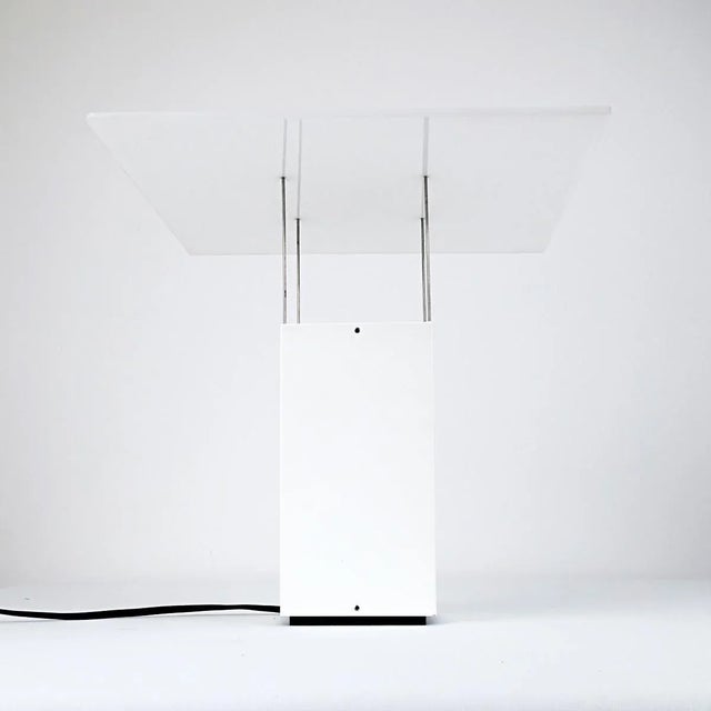 This elegant table lamp has a solid base above which a panel seems to float. The panel, like the base made of white...