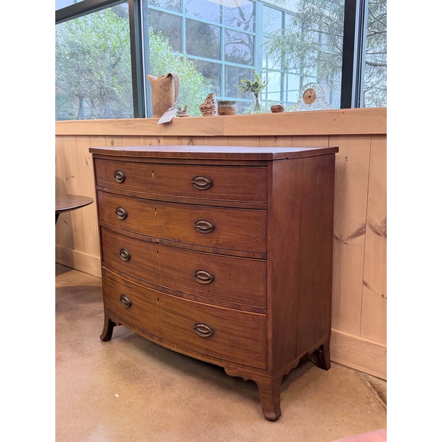 This is an elegant 19th century English bowfront chest of drawers crafted in richly figured mahogany, showcasing a...