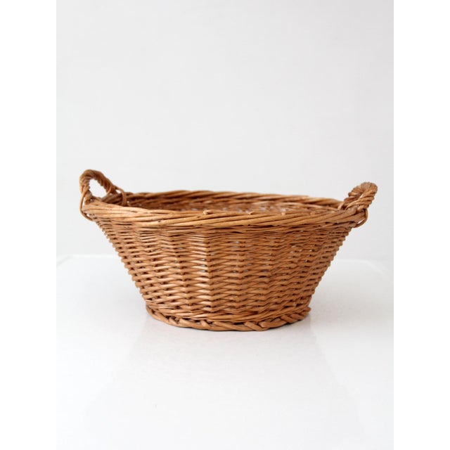 A vintage woven gathering basket with a softly rounded, low open form and integrated side handles. Crafted in natural...