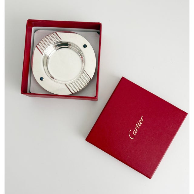 A sophisticated silver-plated catchall or ashtray by Cartier. The rim features fluted rests and two vivid blue lapis...