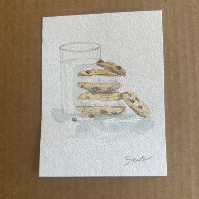 Indulge in the comfort of nostalgia with this delicate watercolor painting featuring a glass of milk alongside a stack of...