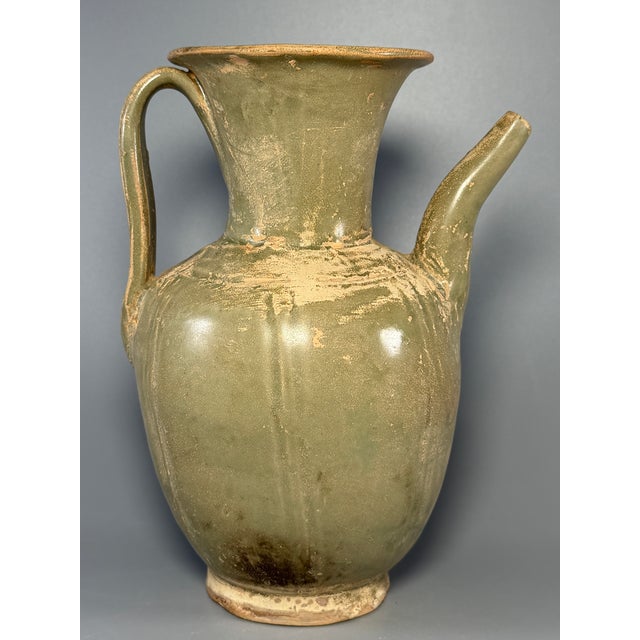 This antique Chinese celadon ewer features elegant spout and curved handle, with natural aged patina on the glaze. A fine...