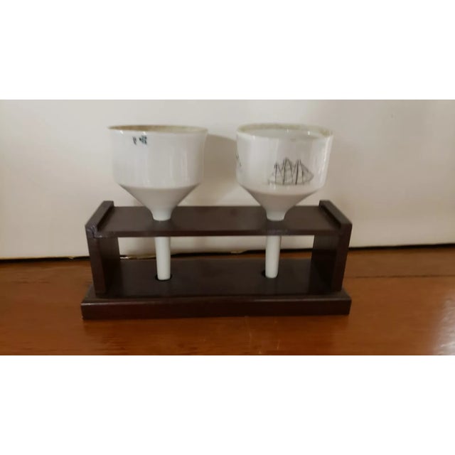This is a Pair of 1970s Coors Porcelain Scrimshaw Style Buchner Funnels in Wooden Stand. The stand measures 9 3/4" long by...
