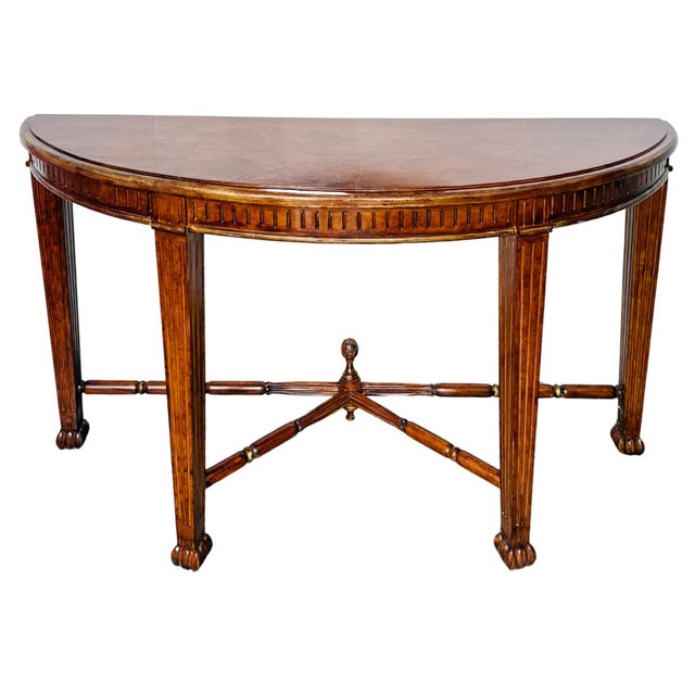 A striking Neoclassical demilune console table with a beautiful, rich wood grain finish and gold leaf accents. Features a...