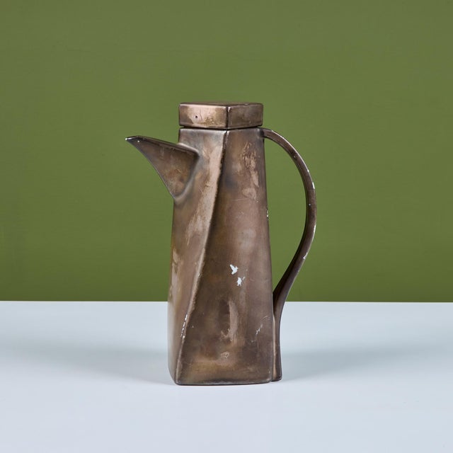 Geometric ceramic pitcher with a faux metal painted exterior. The pitcher features curved handle, spout and lid....