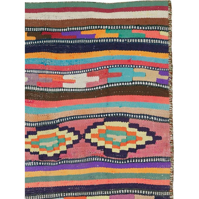 This mid-20th century Persian flatweave kilim rug is a vibrant celebration of tribal color and rhythmic design. Woven in...