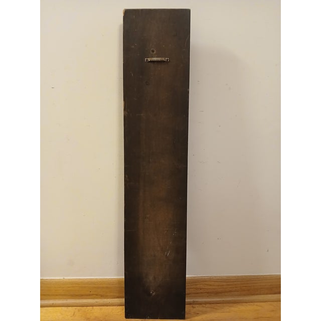 This decorative wall sculpture features a finely carved female figure in flowing classical robes, rendered in rich warm...