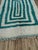 A striking Beni Ourain rug with concentric teal-green rectangles radiating across a plush ivory wool ground. Hand-knotted...
