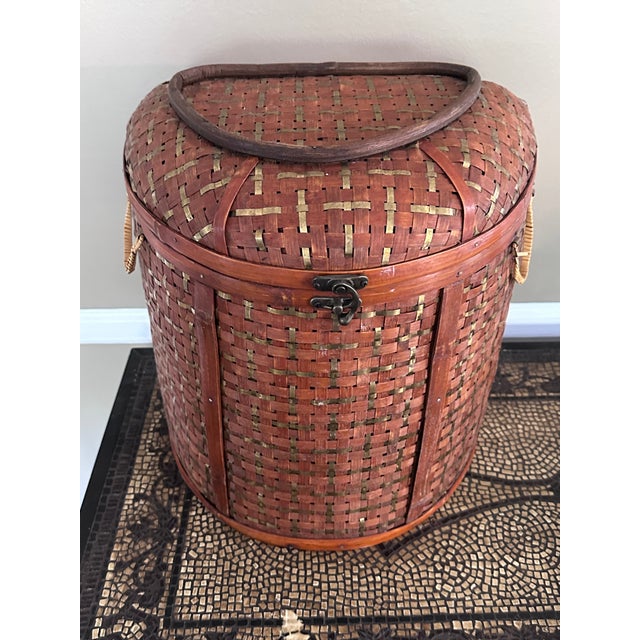 Large decorative basket of woven bamboo with brass accents. Lidded with hardware and handles.