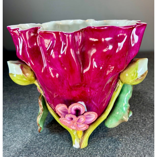 Footed glazed magenta colored vase with green, pink, and yellow fruit/flower theme and a ruffled edge.