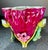 Footed glazed magenta colored vase with green, pink, and yellow fruit/flower theme and a ruffled edge.
