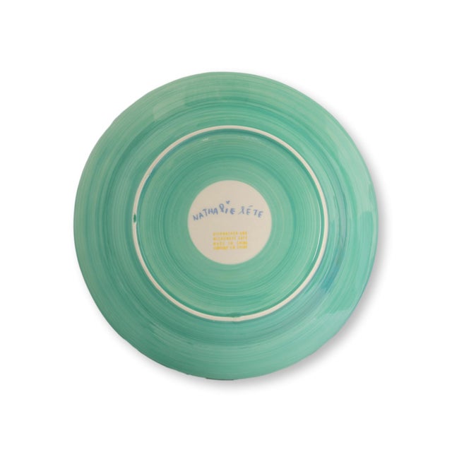 Set of four Nathalie Lété dinner plates featuring whimsical dog portraits and playful French inscriptions in the artist’s...