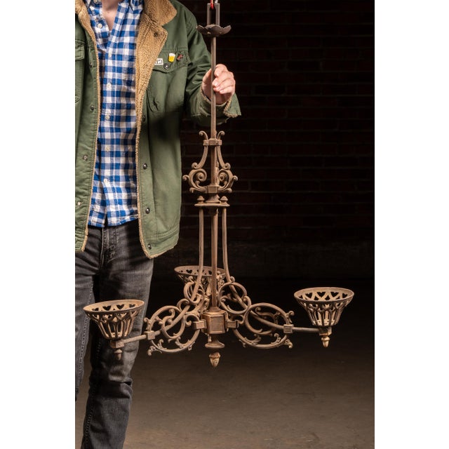 Ornate cast iron chandelier featuring a three-arm configuration with elaborate Gothic Revival detailing throughout. The...