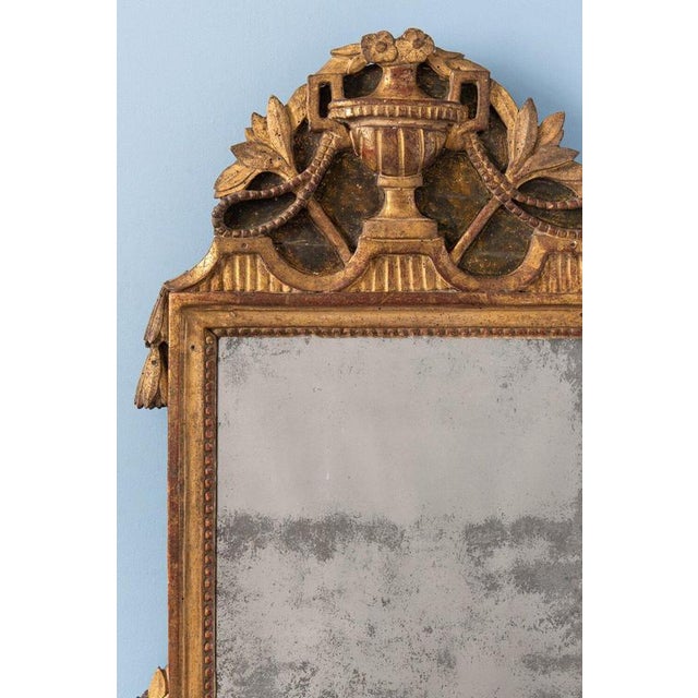 A late 18th-century French giltwood mirror in the Louis XVI style, topped by a striking crest centred on a gadrooned urn...