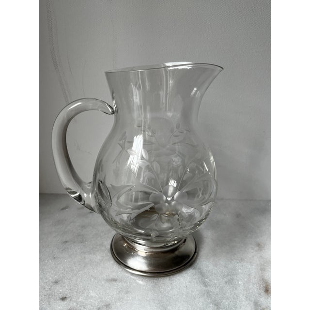 This is an etched crystal pitcher, also known as a "pot belly pitcher," with a sterling silver base. The etching on the...