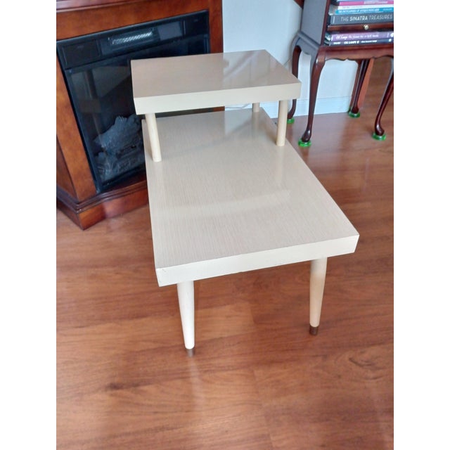 Vintage 1950's Mid Century 2 Tier Blonde Step Table with Laminated Top and Tapered Gold Tone Tipped Legs. This table is in...