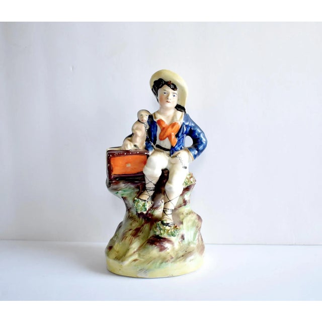 An antique Staffordshire figurine of a boy in a blue coat with a monkey and organ grinder, seated on a log; with bocage....
