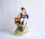 An antique Staffordshire figurine of a boy in a blue coat with a monkey and organ grinder, seated on a log; with bocage....