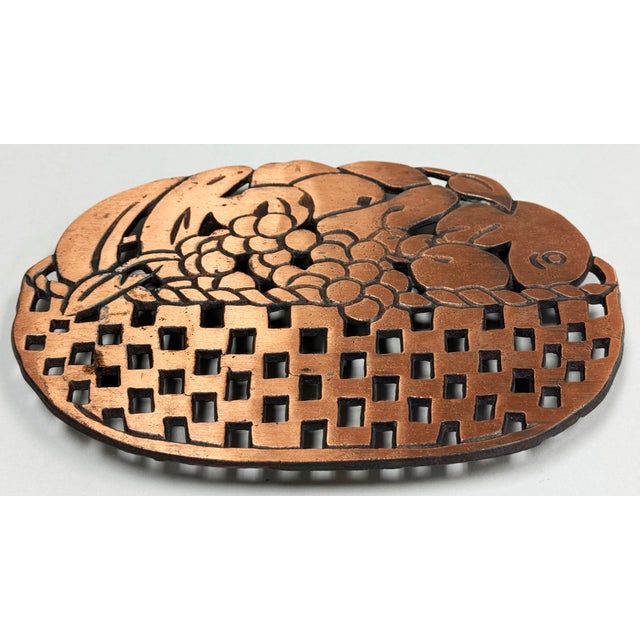 Vintage copper and cast iron basket of fruit motif trivet. Hanging hardware on the back and rubber pads to the feet....