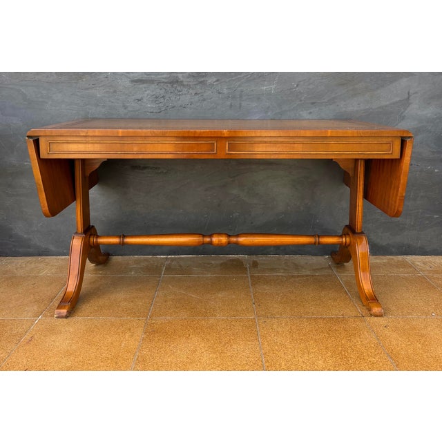 Elegant drop-leaf low table dating to the mid-20th century. The table features a rectangular top with a leather writing...