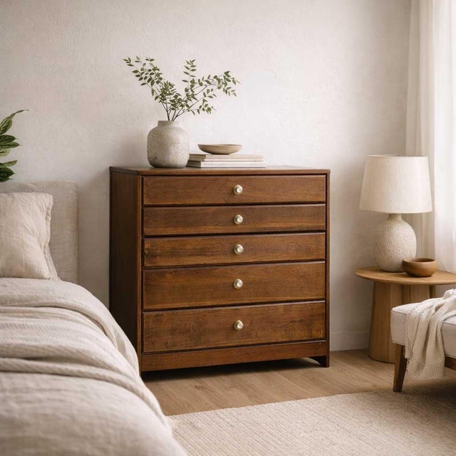 A compact vintage mid-century chest of drawers with warm walnut-toned grain, six flush-front drawers, and understated...
