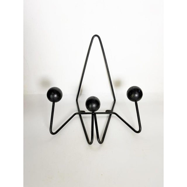 A vintage wall-mounted coat rack in black lacquered metal, featuring the minimalist, graphic design typical of the 1960s....