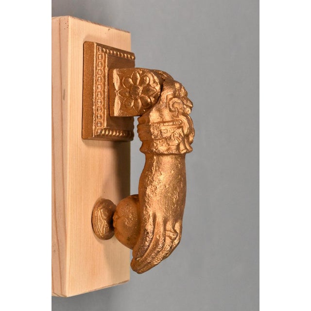 A gilt cast iron door knocker in the form of the hand of Fatima. The piece is decorated with foliage and the hand holds a...