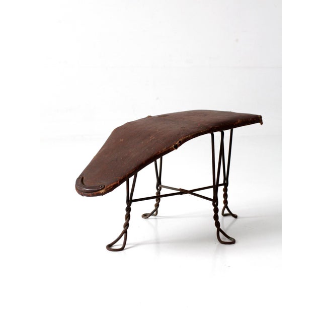 This antique Victorian shoe fitting stool features a twisted iron base, sloped upholstered top, and metal heel stop....