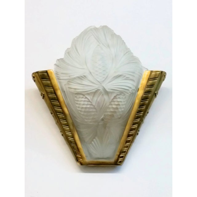 A pair of French Art Deco wall sconces in molded clear frosted glass with pine cone motif with polished details. Resting...