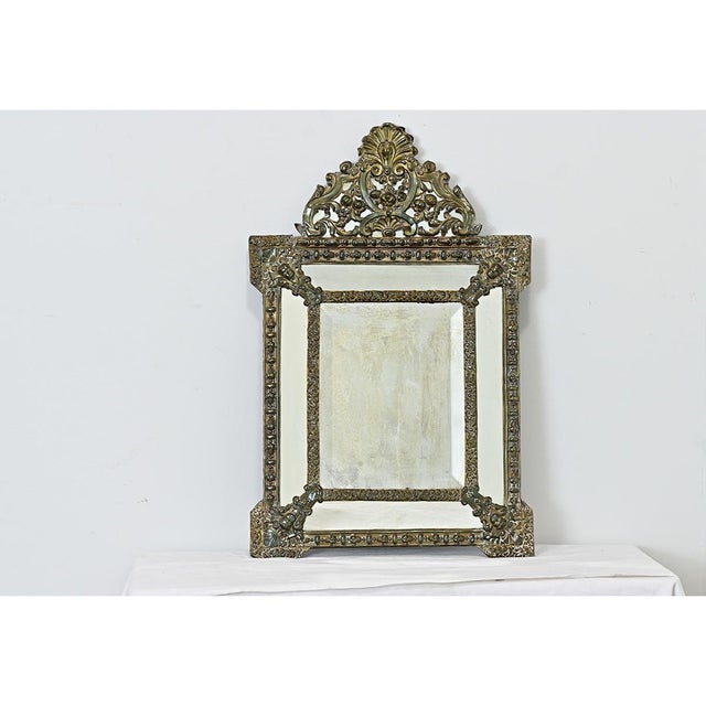 A fantastic cushion mirror in répoussé brass on wood backing, from the 19th century. This petite mirror features ornate...