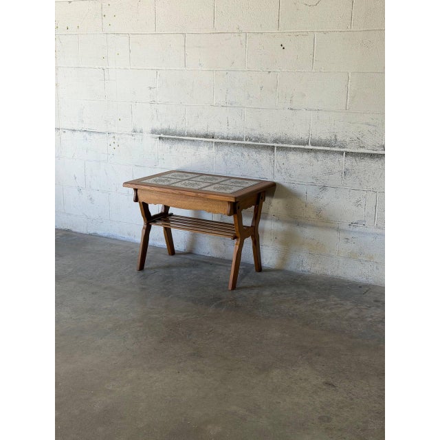 This vintage coffee table features an inset ceramic tile top with stylized floral motifs set within a rich oak frame....