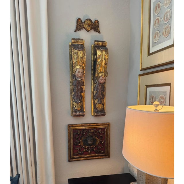 A richly detailed three-dimensional carved wood panel featuring a central cherub face with wings, surrounded by scrolling...