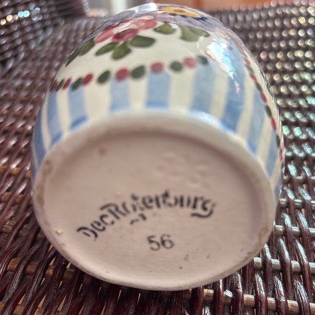 The vase is hand-painted with a vibrant floral motif featuring blue/purple, pink, and yellow flowers on a cream background...