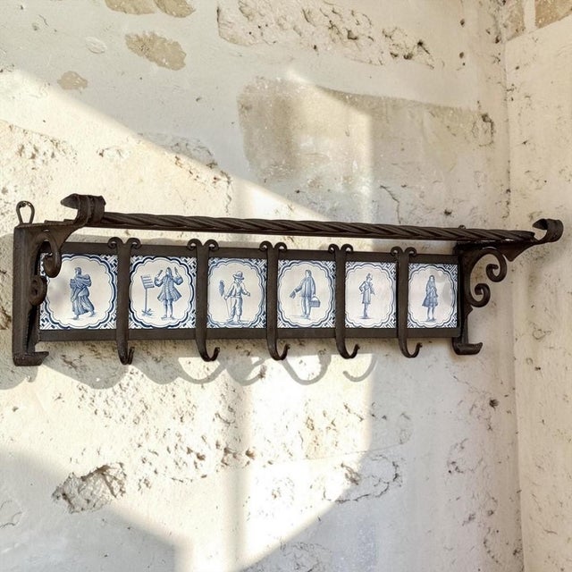 A charming marriage of Dutch ceramic art and hand-forged ironwork, this 19th century wall-mounted coat rack features six...